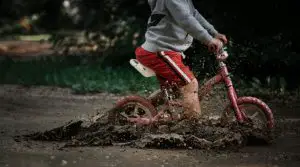 Photo of a young boy riding a balance bike through a muddy puddle